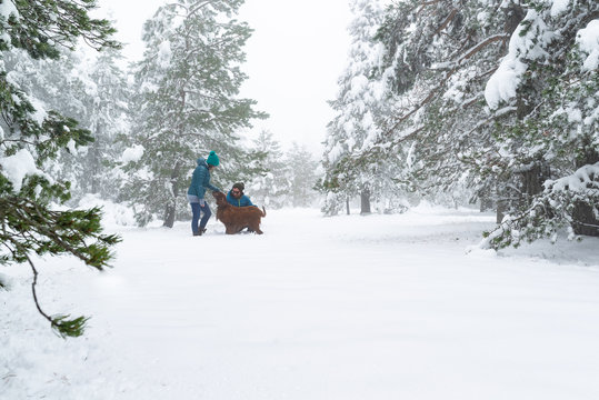 Pareja feliz jugando con su perro en un bosque nevado. Disfrutando el invierno.