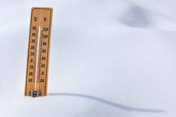 Wooden thermometer standing in the snow, sun casting curvy shadow, red column showing 0 degrees...