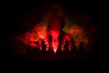 Man playing chess. Scary blurred silhouette of a person at the chessboard with chess figures. Dark toned foggy background.