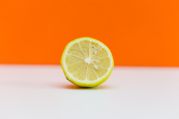 close-up of a Single half lemon citrus fruit, white surface against orange background