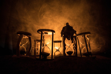 Time concept. Silhouette of a man standing between hourglasses with smoke and lights on a dark...