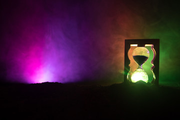 Time concept. Silhouette of Hourglass clock and smoke on dark background with hot yellow orange red blue cold back lighting, or symbols of time