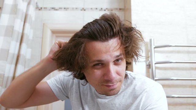 Young shaggy man combs hair with a comb arter head washing.