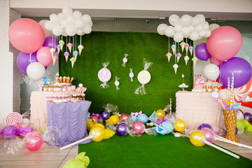 Birthday party concept, decorations for sweet party. Huge number one, table with sweets and desserts, cloud from balloons and ice-creams, a lot of colored balloons and big candy toys