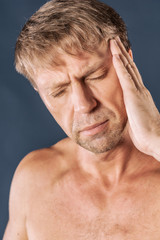 A man holds his hands on his head on blue background. Headache or migraine.