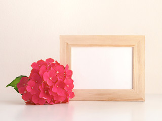 Hydrangea flower and blank photo frame on table in front of the wall.