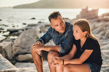 Father and daughter sitting on a rocky beach and talking