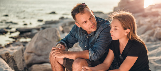 Father and daughter sitting on a rocky beach and talking