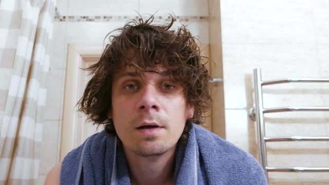 Young shaggy man combs hair with a comb arter head washing.