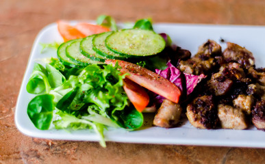 tasty dish with pork, lettuce, tomato and cucumber on a white plate with a dip