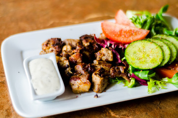 tasty dish with pork, lettuce, tomato and cucumber on a white plate with a dip