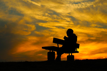 夕暮れの丘でベンチに座る女性