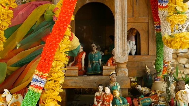 Wooden miniature guardian spirit house. Small buddhist temple shrine, colorful flower garlands. San phra phum erected to bring fortune. Traditional respect animistic rituals, pray ceremonies