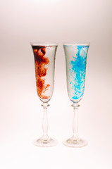 The effect of water smoke using an red and blue food coloring in two glasses for champagne on a white background.