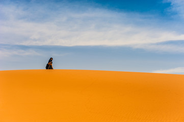 Fototapeta na wymiar old berber woman walking alone on a sand dune in Merzouga, Morocco