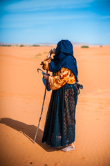 old  berber woman walking alone on a sand dune in Merzouga, Morocco