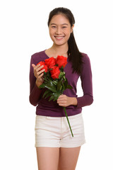 Young happy Asian teenage girl smiling holding red roses ready f