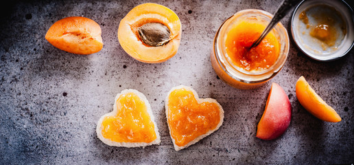 Apricot jam and heart shaped toasted bread on a rustic background - banner - header