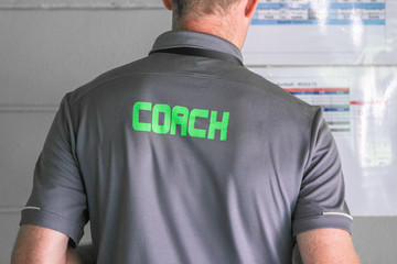 Back view of male sport coach with word COACH written on back of his shirt