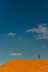 Naklejka na ściany i meble Girl stands on the dune erg chebbi and observes the desert landscape in merzouga morocco