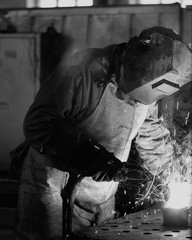 Welder at the factory in a welding mask welds metal parts, welding and sparks, black and white, industrial