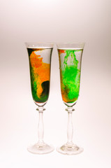 The effect of water smoke using an orange and green food coloring in two glasses for champagne on a white background.