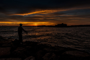 Fototapeta premium Fisherman catches fish at sunset