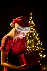 Young woman with gift, Christmas tree and decorative lighting bokeh background. Elf and spruce with decorations. Girl and adornment.