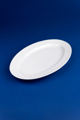 Ceramic white oval plate with board on blue background. Mock up for design.