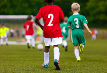 Obraz premium Multiracial kids kicking football on the sports field. An action sport picture of a group of kids playing soccer football tournament game. Two running soccer players in the foreground