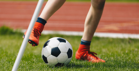 Close-up of Young Soccer Player Kicking Ball on Soccer Field. Football Corner Kick on the Pitch. Footballer in Red Cleats on the Green Lawn of the Stadium