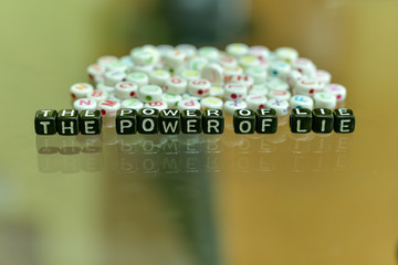 THE POWER OF LIE written with Acrylic Black cube with white Alphabet Beads on the Glass Background