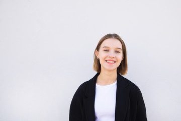 Happy, attractive young woman in a suit on a white background looks at the camera and smiles....