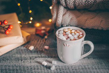 Stack of cozy knitted sweaters and cup of coffee or hot chocolate with marshmallow on wooden background. Autumn-winter concept. Magic, cozy and mood time