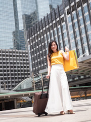 The asian woman hold the shopping bag and bag in the city. Her face happy with smile