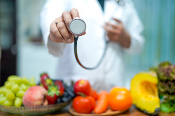 Nutritionist doctor holding orange juice with strawberry, potatoes, apples, plum, grapes, carrot, peach, pumpkin and salad vegetable on desk to instruction healthy food strong patient.