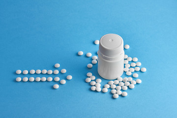 Arrow made from white medical round pills on blue background.