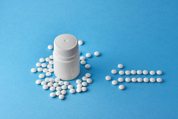 Arrow made from white medical round pills on blue background.