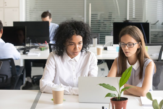 Serious diverse african american and caucasian office colleagues discussing online project result working together sharing ideas helping in brainstorm looking at laptop screen, mentor teaching intern