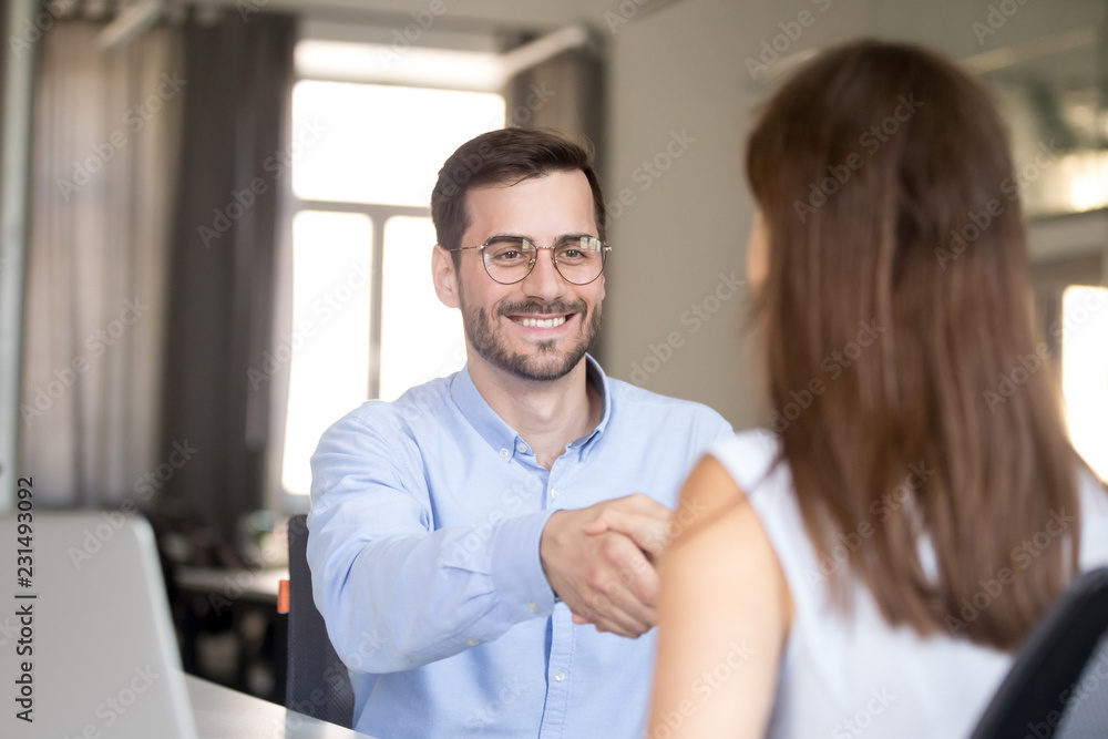 Wall mural smiling attractive millennial friendly businessman handshaking woman at job interview, happy employe