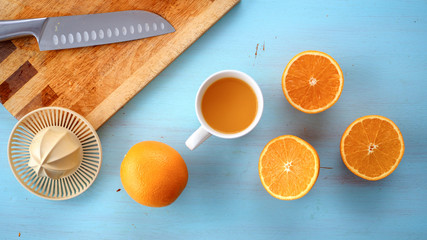 Fototapeta Świeży wyciśnięty sok z pomarańczy leżący w towarzystwie wyciskarki, noża oraz pomarańczy na drewnianej desce obraz