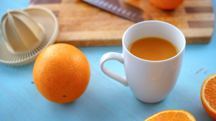 Świeży wyciśnięty sok z pomarańczy leżący w towarzystwie wyciskarki, noża oraz pomarańczy na drewnianej desce - obrazy, fototapety, plakaty