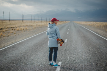 Fototapeta premium Young sporty girl with longboard is standing on a deserted road
