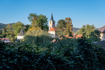 a white church tower and a house with a red roof in a green garden