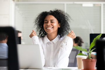 Excited african office worker student receiving good news in email on laptop, motivated happy black...