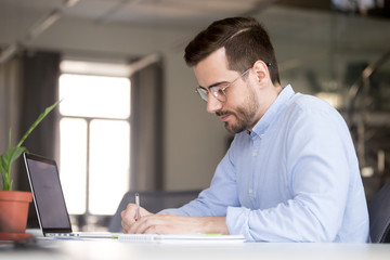 Focused business man making notes planning marketing economic research work with laptop, serious...