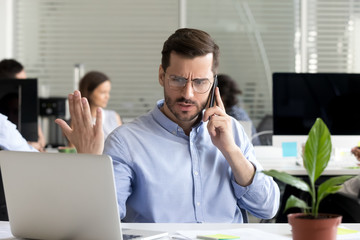 Angry business man talking on phone disputing looking at laptop, stressed frustrated office worker...