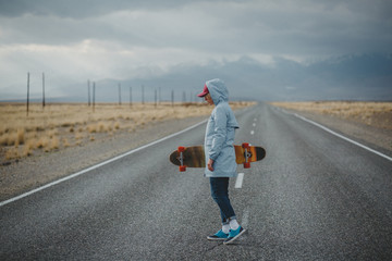 Obraz premium Young sporty girl with longboard is standing on a deserted road