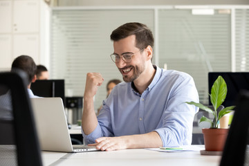 Excited motivated male worker happy by receiving good news in email looking at laptop, lucky business man winning online, getting promotion, celebrating success profit, satisfied with great result