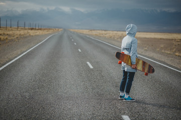 Young sporty girl with longboard is standing on a deserted road